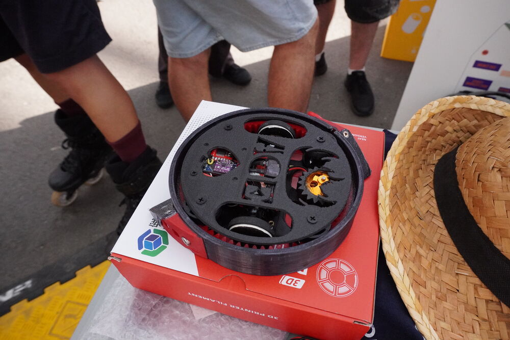 Un robot negro con forma de disco sobre su caja, junto a un sombrero de paja