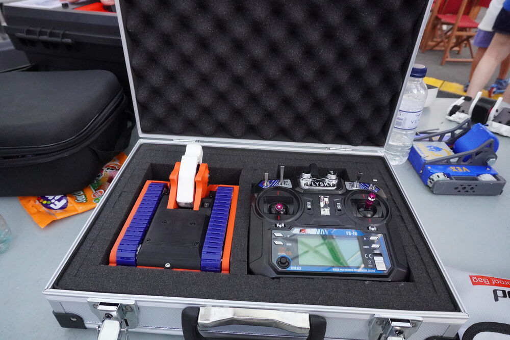 Un robot naranja con orugas azules en su maletín de espuma junto a la emisora