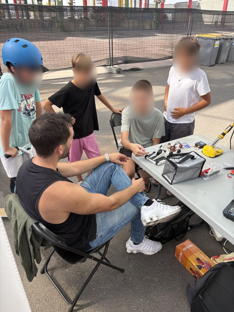 Tres niños con cascos rodean a un piloto sentado a la mesa del pit
