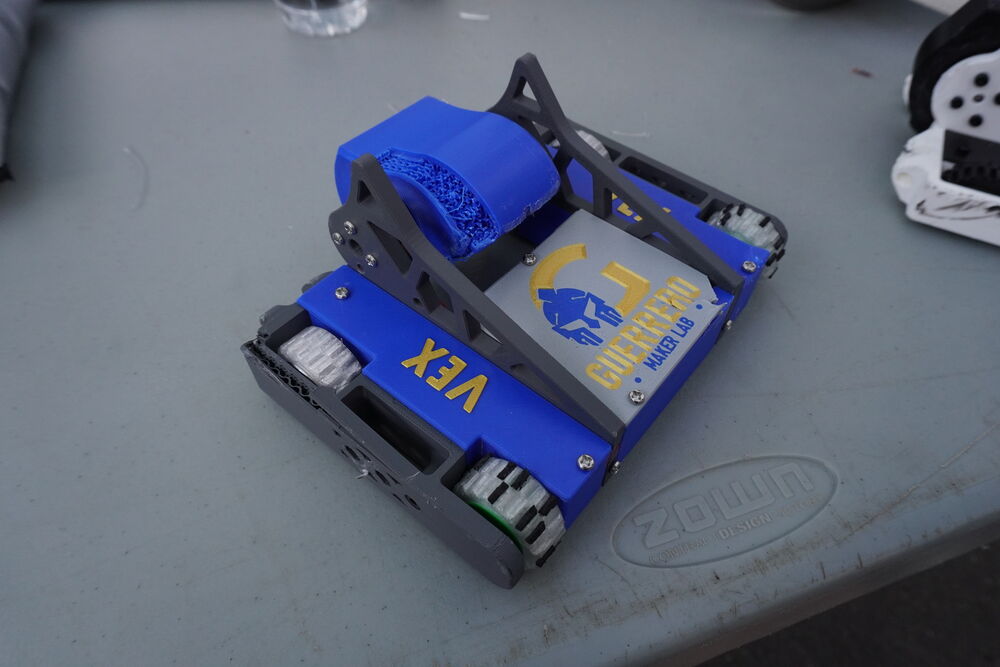 Vex, un robot de orugas azul con un brazo elevador, sobre la mesa del pit